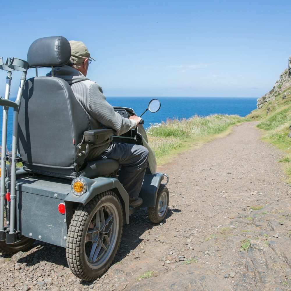 senior man riding a mobility scooter or tramper over rough terrain in an independence concept image